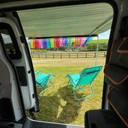 View from inside a vehicle showing turquoise chairs on grass with colourful bunting in the background.