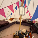 Inside a bell tent with beds, pillows, and a mirror against a colourful bunting backdrop.