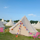Bell tents with colourful flags on a grassy field under a clear blue sky