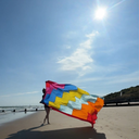Person holding a colourful flag on a sandy beach with a clear blue sky.