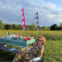 Woman sitting at a picnic table in a field with colourful flags in the background