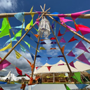 Colourful triangle bunting and a teepee structure against a blue sky with tents in the background