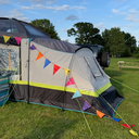 Camping tent with colourful bunting attached in a grassy area with trees in the background.
