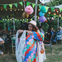 Two women hugging at an outdoor event with colorful decorations and people in the background.