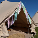 Beige bell tent with pastel-coloured tassels against a blue sky