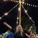 Woman celebrating under a decorated pole with lights and bunting at a festival
