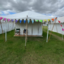 White bell tent with colourful bunting on a grassy field under a cloudy sky