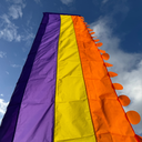 Rainbow flag with purple, orange, and yellow sections against a blue sky.