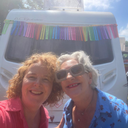 Two women standing in front of a white campervan with rainbow bunting on a sunny day.