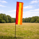Red and yellow flag on a pole in a grassy field with trees in the background
