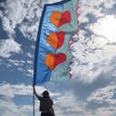 Person holding a colourful kite with heart designs against a blue sky with clouds