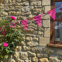 Pink bunting on a stone wall with pink flowers and a window.