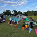 People enjoying a picnic in a field with colourful bunting and a tent.